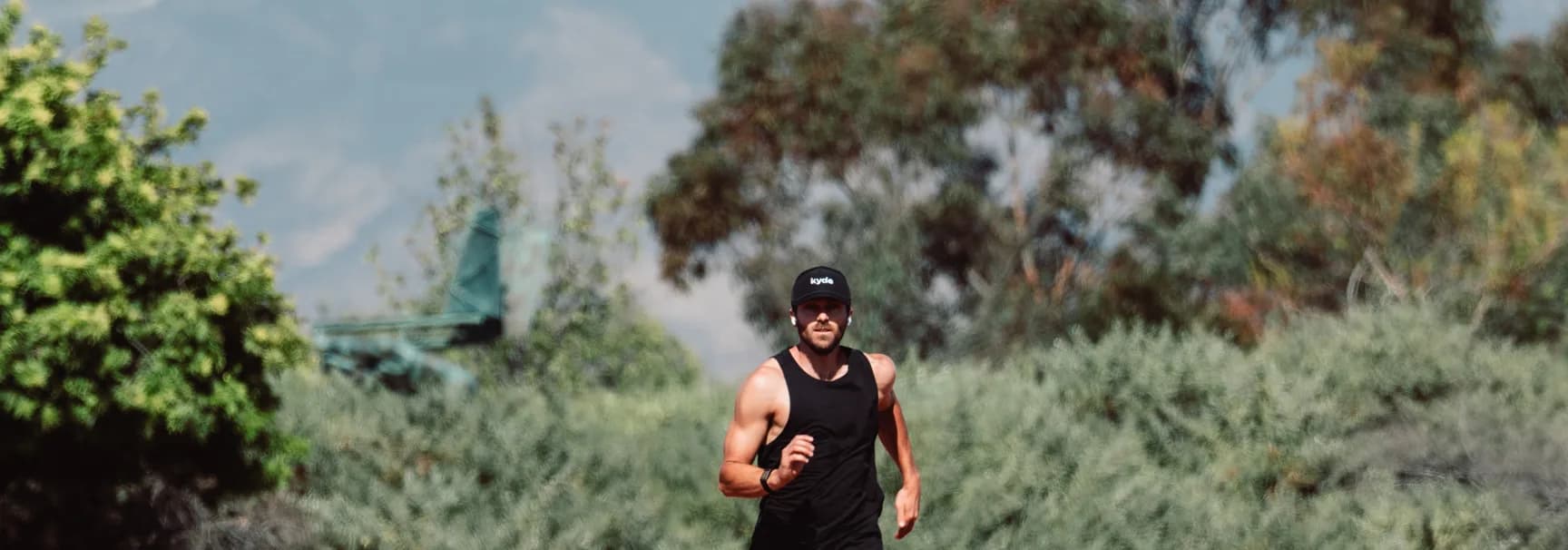 Runner in a kyde cap on a trail, mountains behind